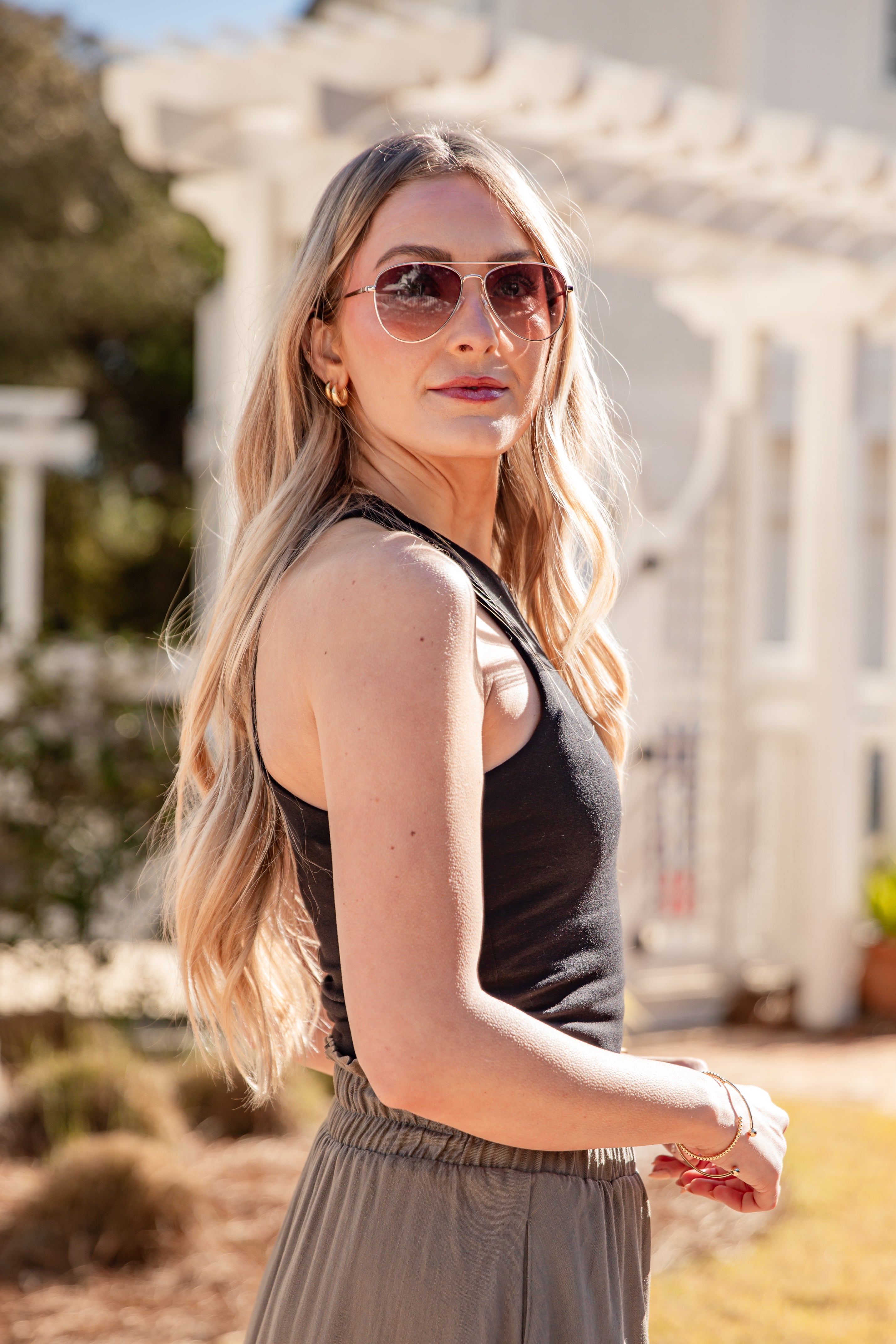 Woman wearing sunglasses and a black top with a blurred outdoor background
