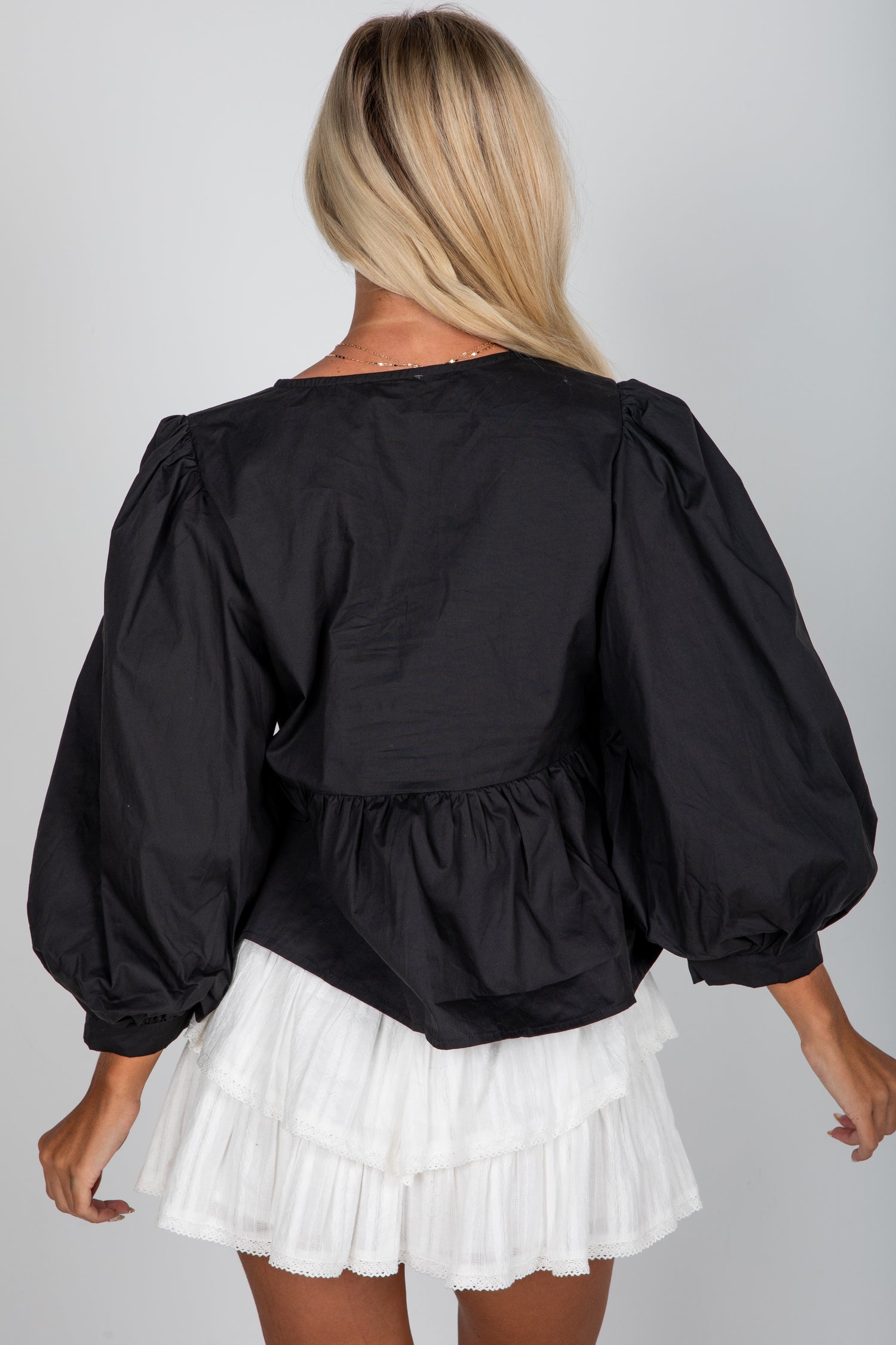 Person wearing a black blouse with puffed sleeves and a white skirt on a plain background