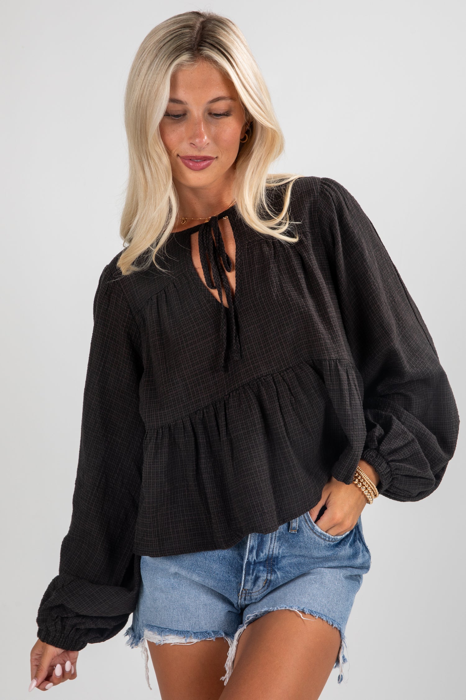 Woman wearing a black blouse and denim shorts on a plain background