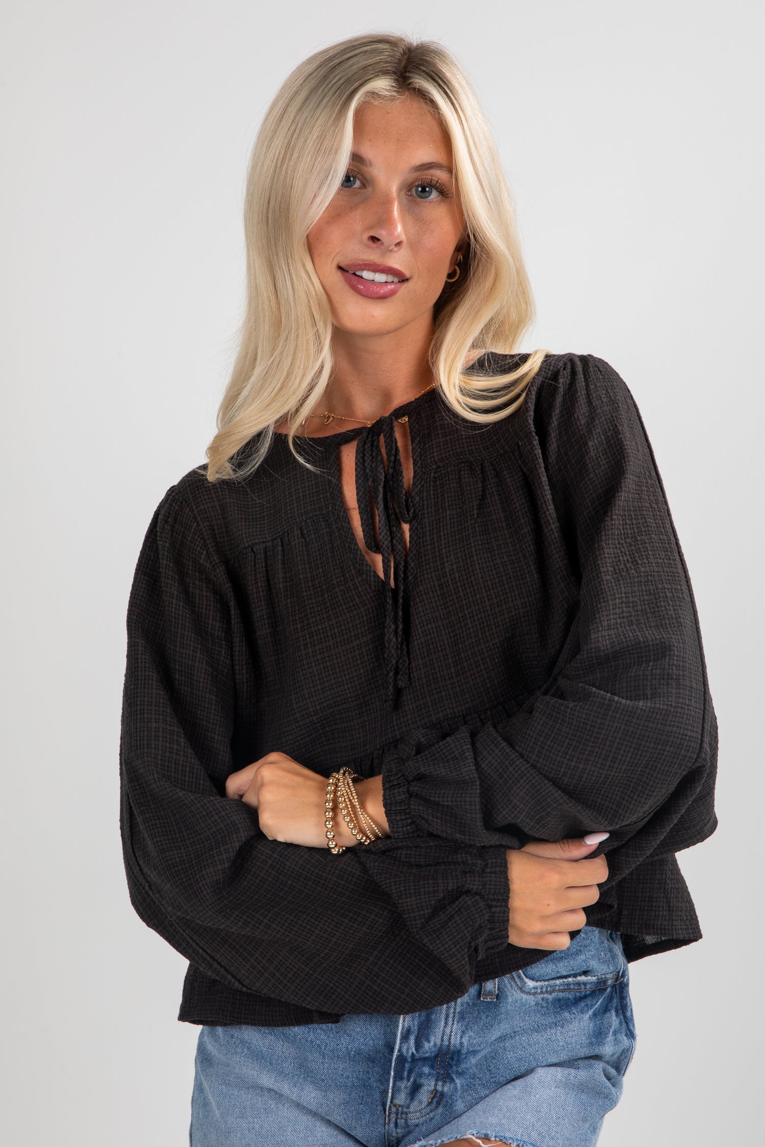Woman wearing a black blouse with long sleeves and blue jeans on a white background