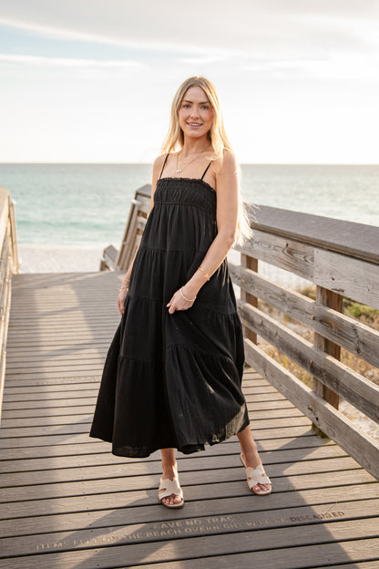Woman in a black dress standing on a wooden pier by the ocean.