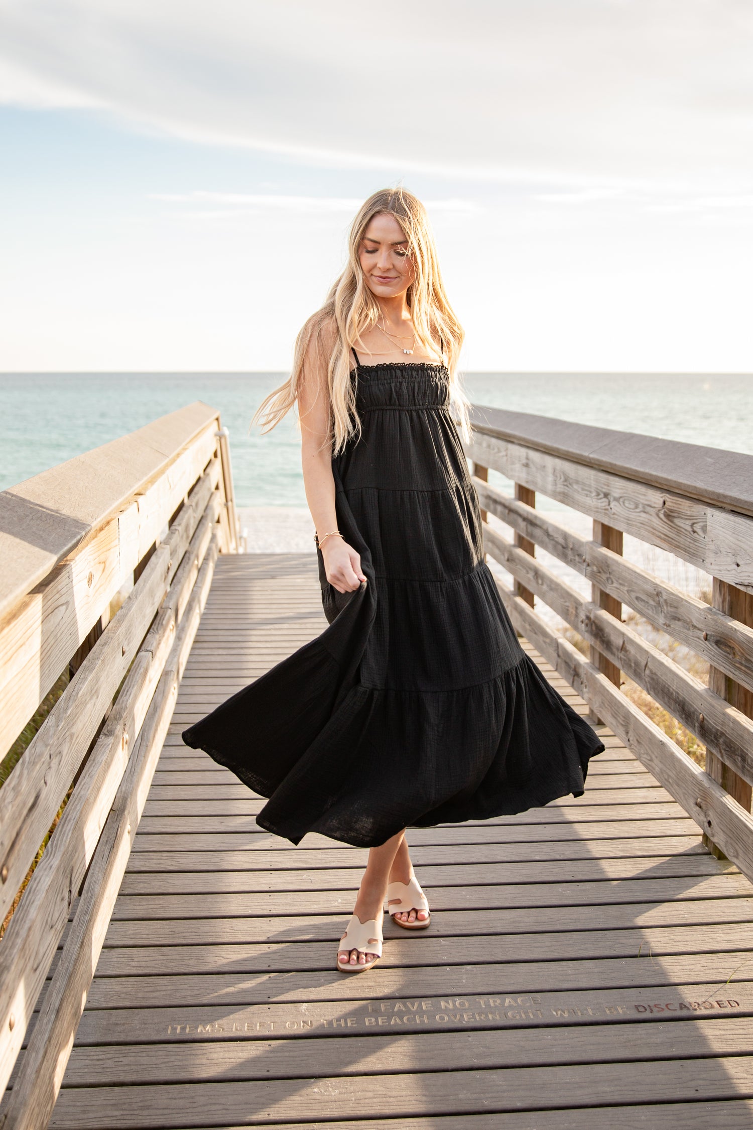 Woman in a black dress standing on a wooden pier by the ocean