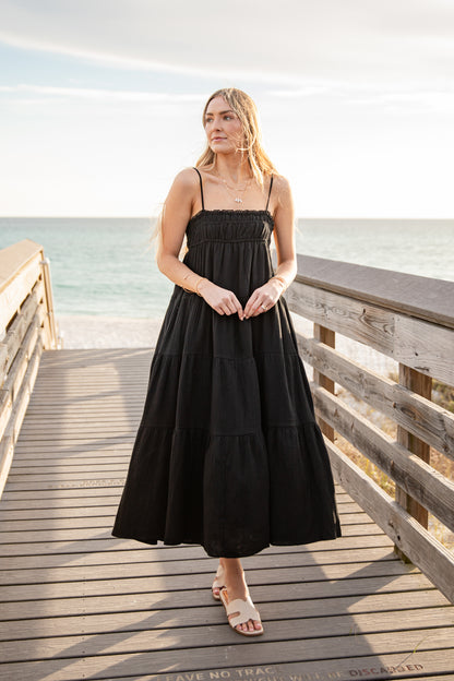 Woman in a black dress standing on a wooden pier by the ocean