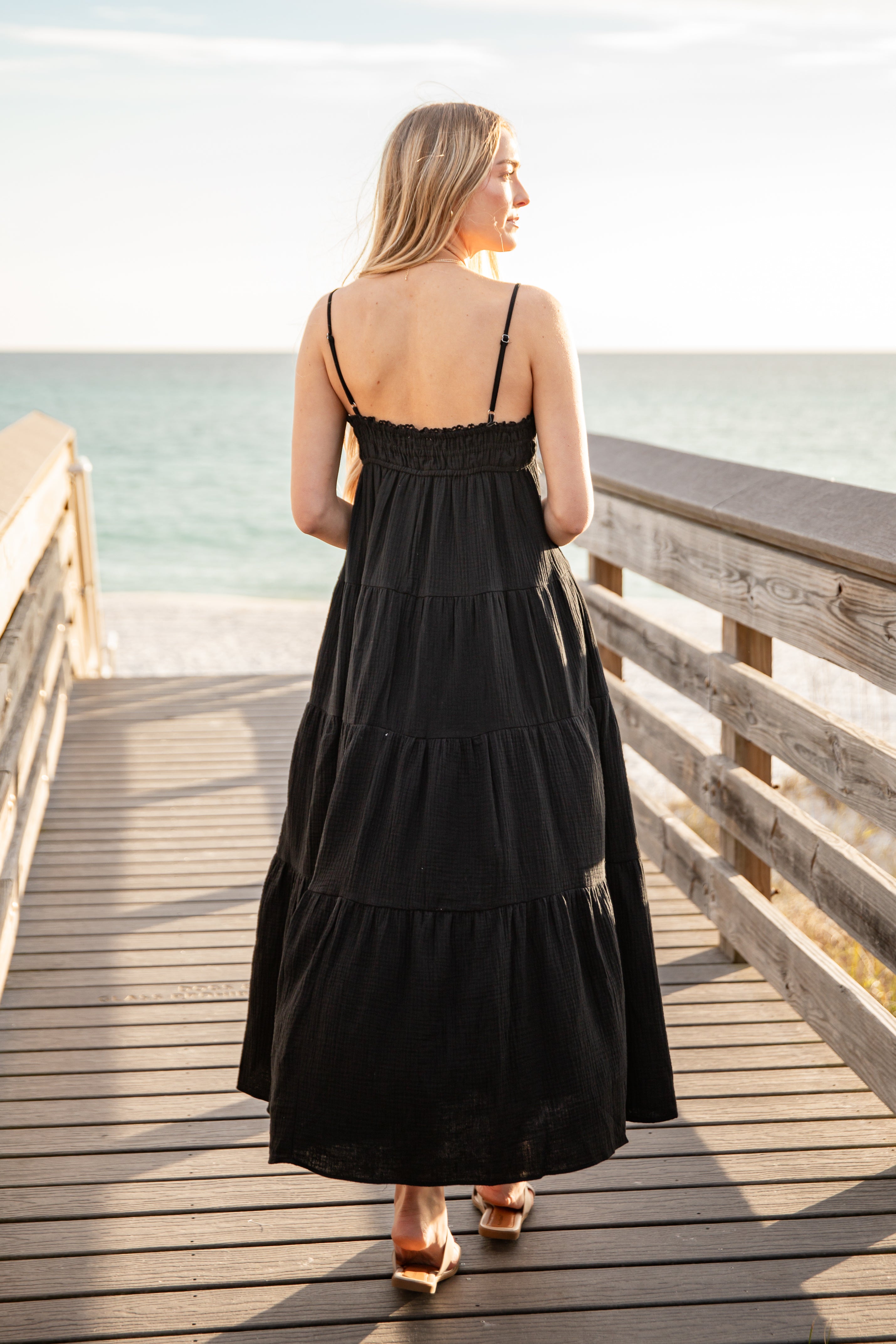 Woman in a black dress standing on a wooden pier by the ocean.