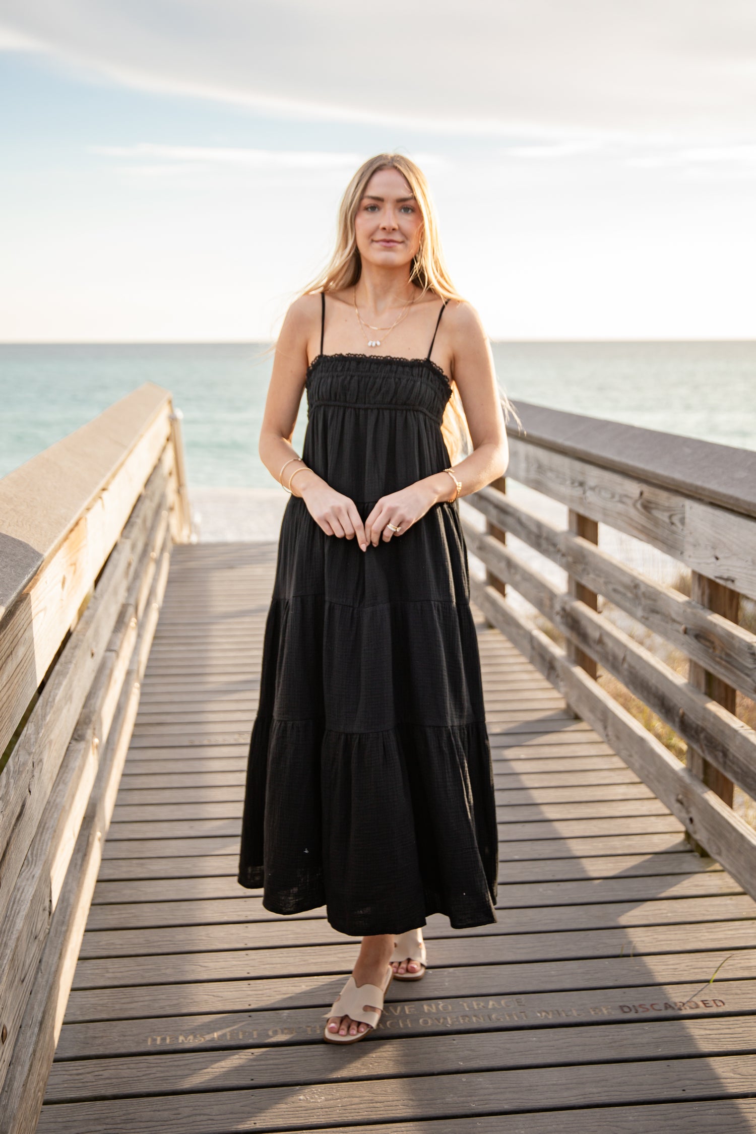 Woman in a black dress standing on a wooden pier by the ocean.