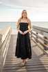 Woman in a black dress standing on a wooden pier by the ocean.