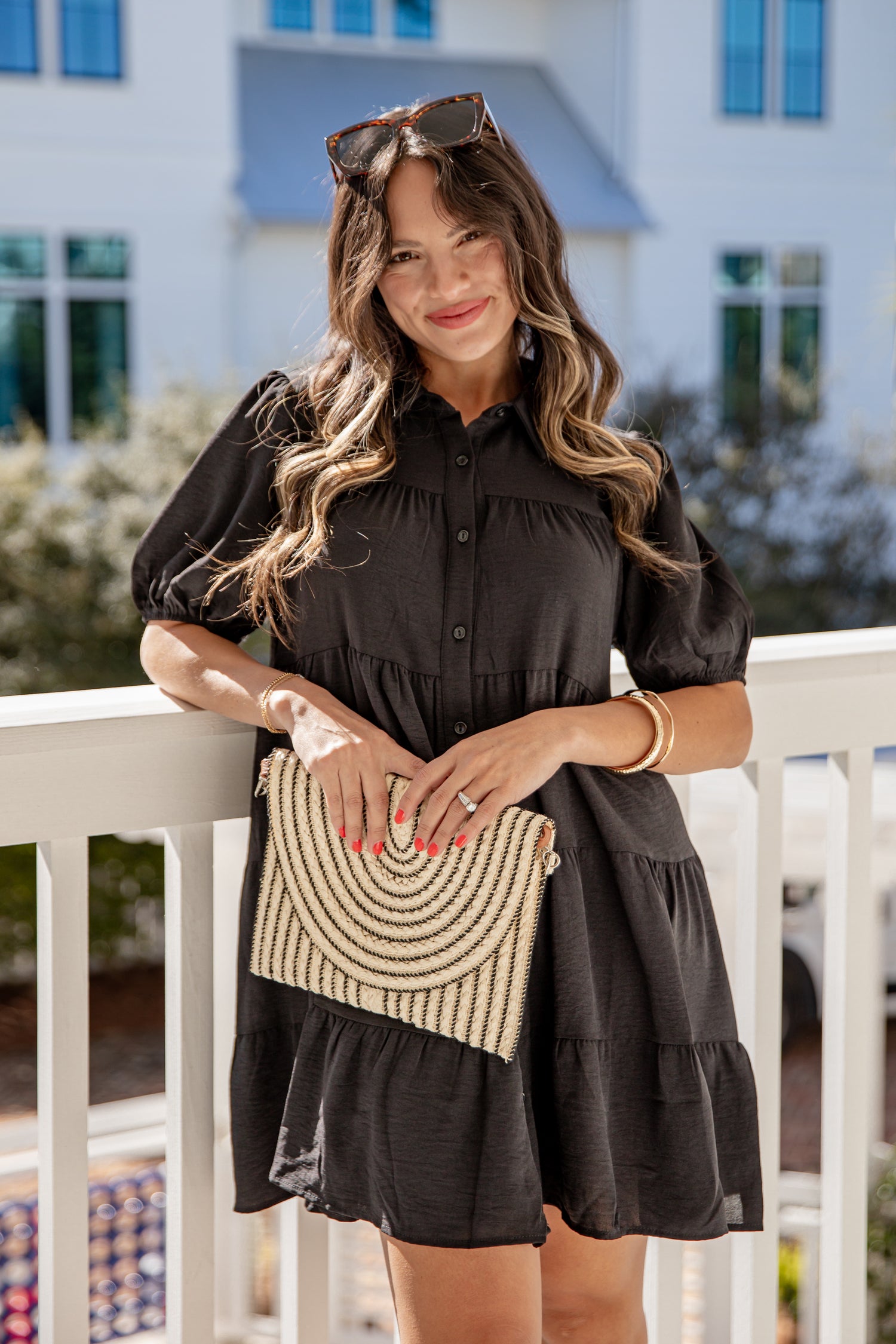 Woman in a black dress holding a beaded handbag on a balcony.