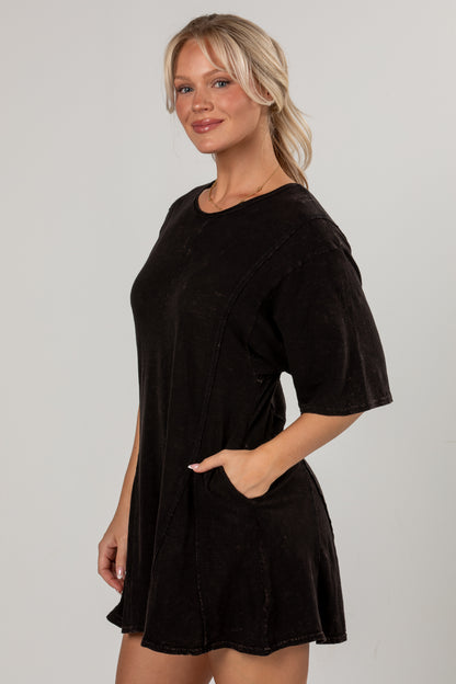 A woman modeling a short-sleeve black corduroy mini romper with side pockets, photographed against a neutral light gray studio background.