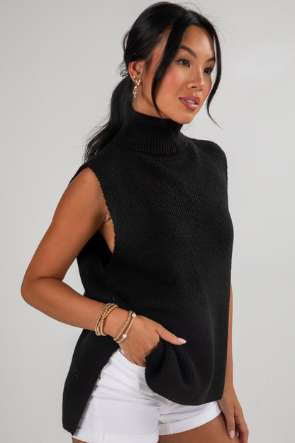 Woman wearing a black sleeveless sweater and white shorts on a plain background