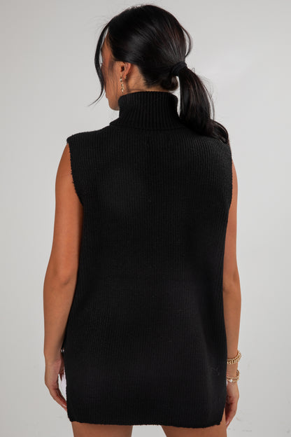 Woman wearing a black sleeveless sweater dress against a plain background