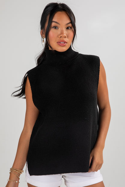 Woman wearing a black sleeveless knit top against a plain background