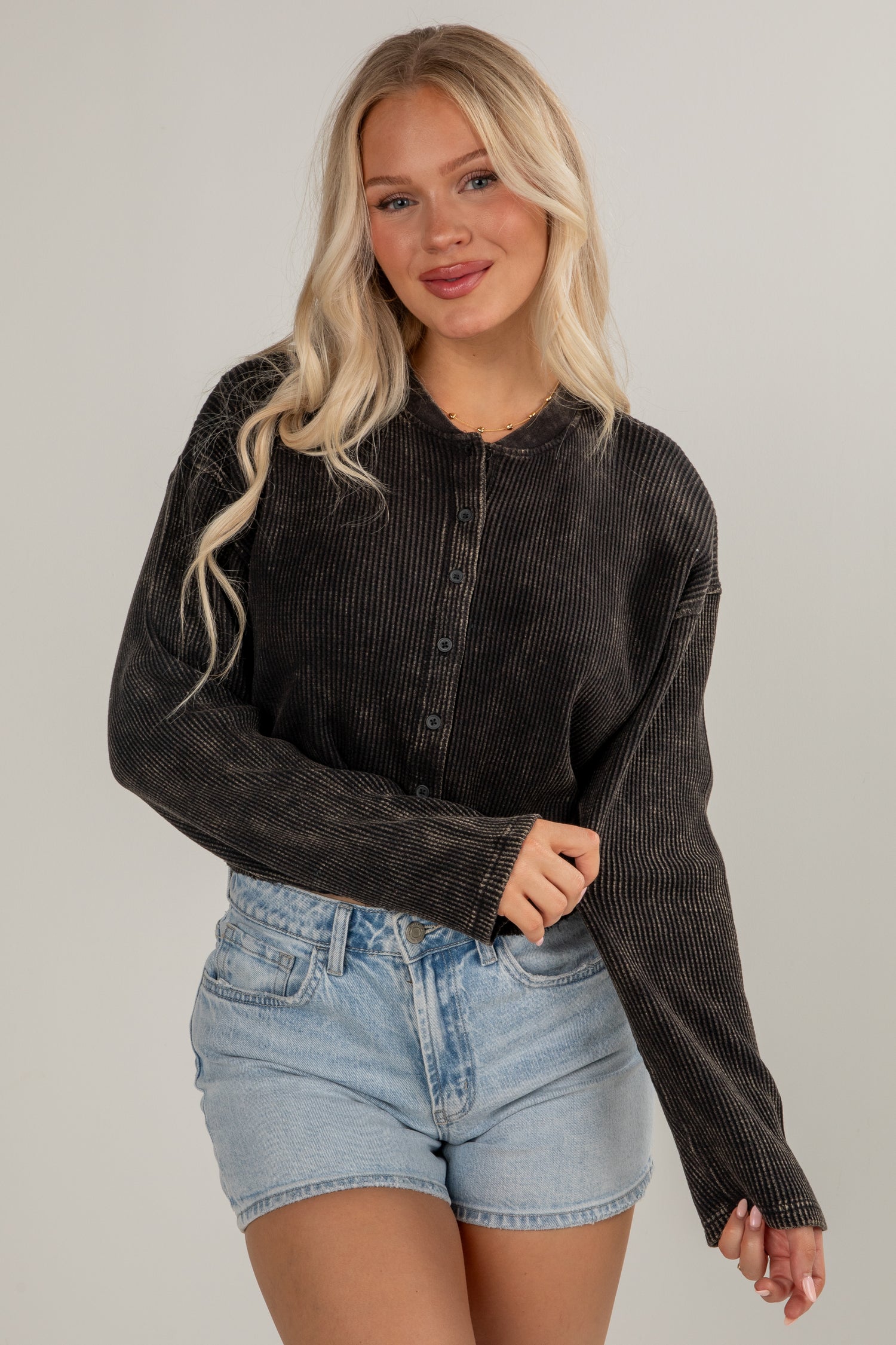 Woman wearing a black ribbed sweater and denim shorts on a plain background