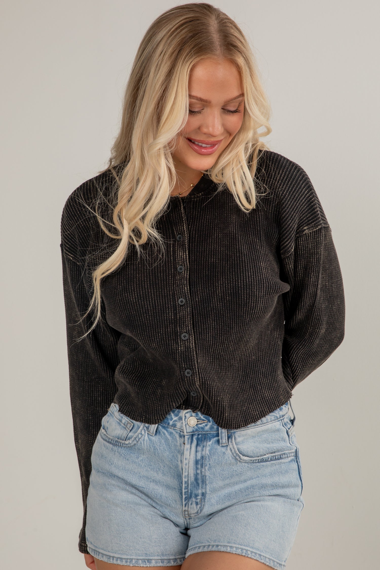 Woman wearing a black corduroy jacket and denim shorts on a plain background
