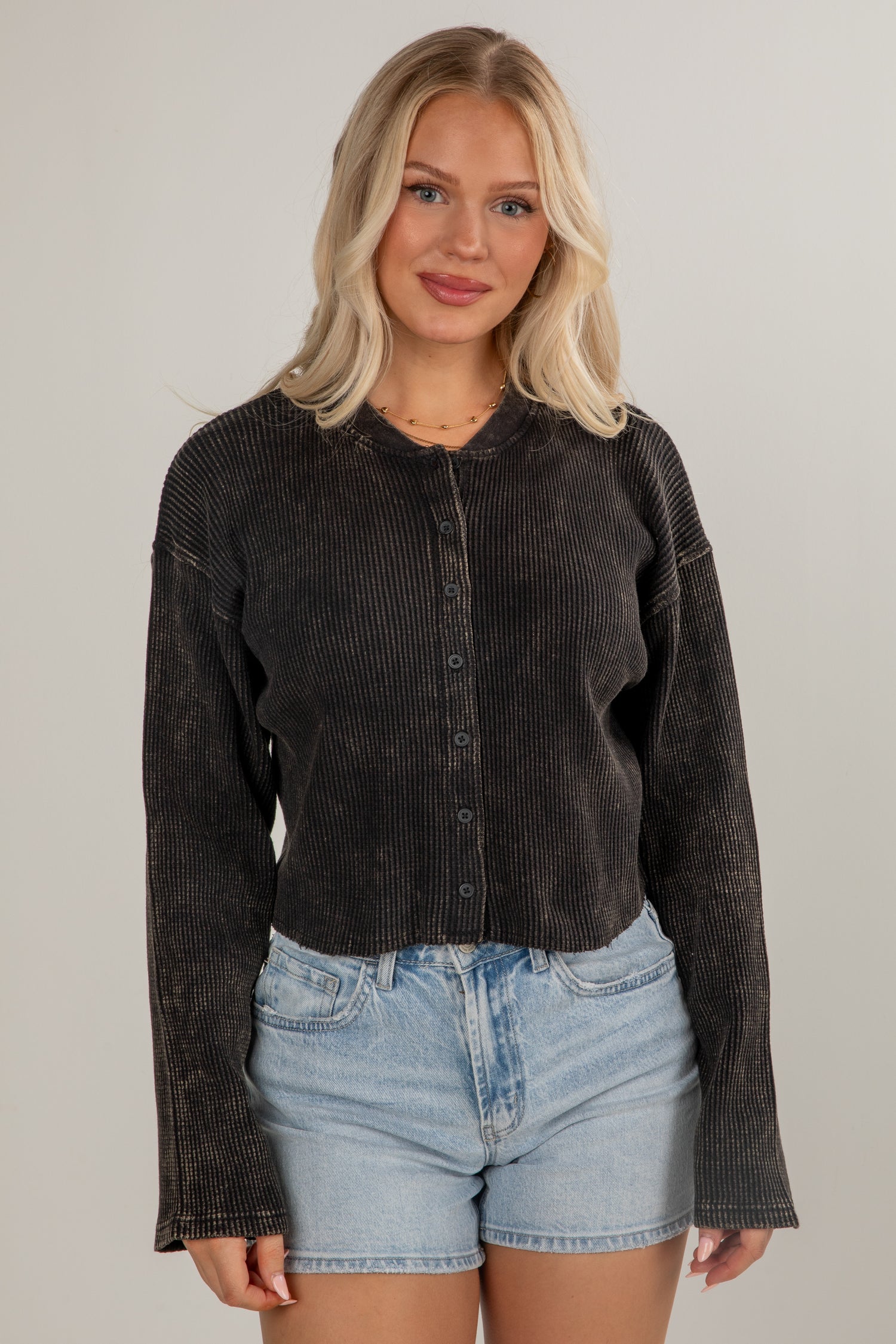 Woman wearing a dark corduroy shirt and denim shorts against a plain background
