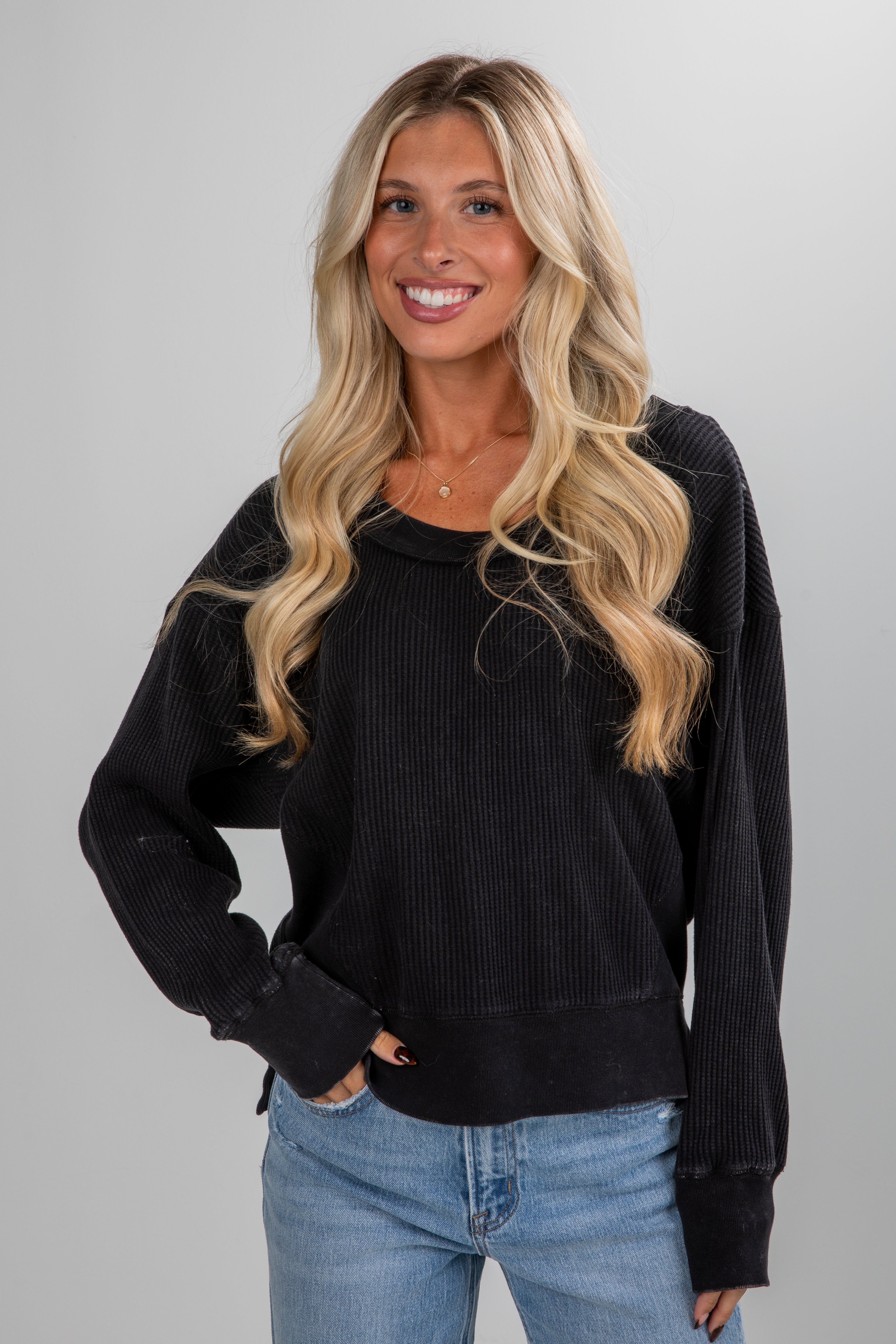 Woman wearing a black sweater and blue jeans against a gray background