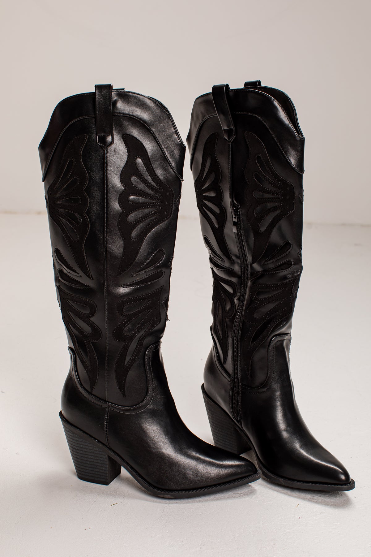 A pair of black leather knee-high cowboy boots with pointed toes, low block heels, and decorative western-style stitching, shown against a plain light background.