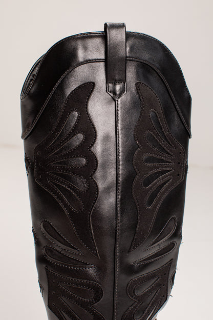 Close-up of a black leather cowboy boot shaft with decorative cutout stitching and a pull tab at the top, photographed against a plain light background.