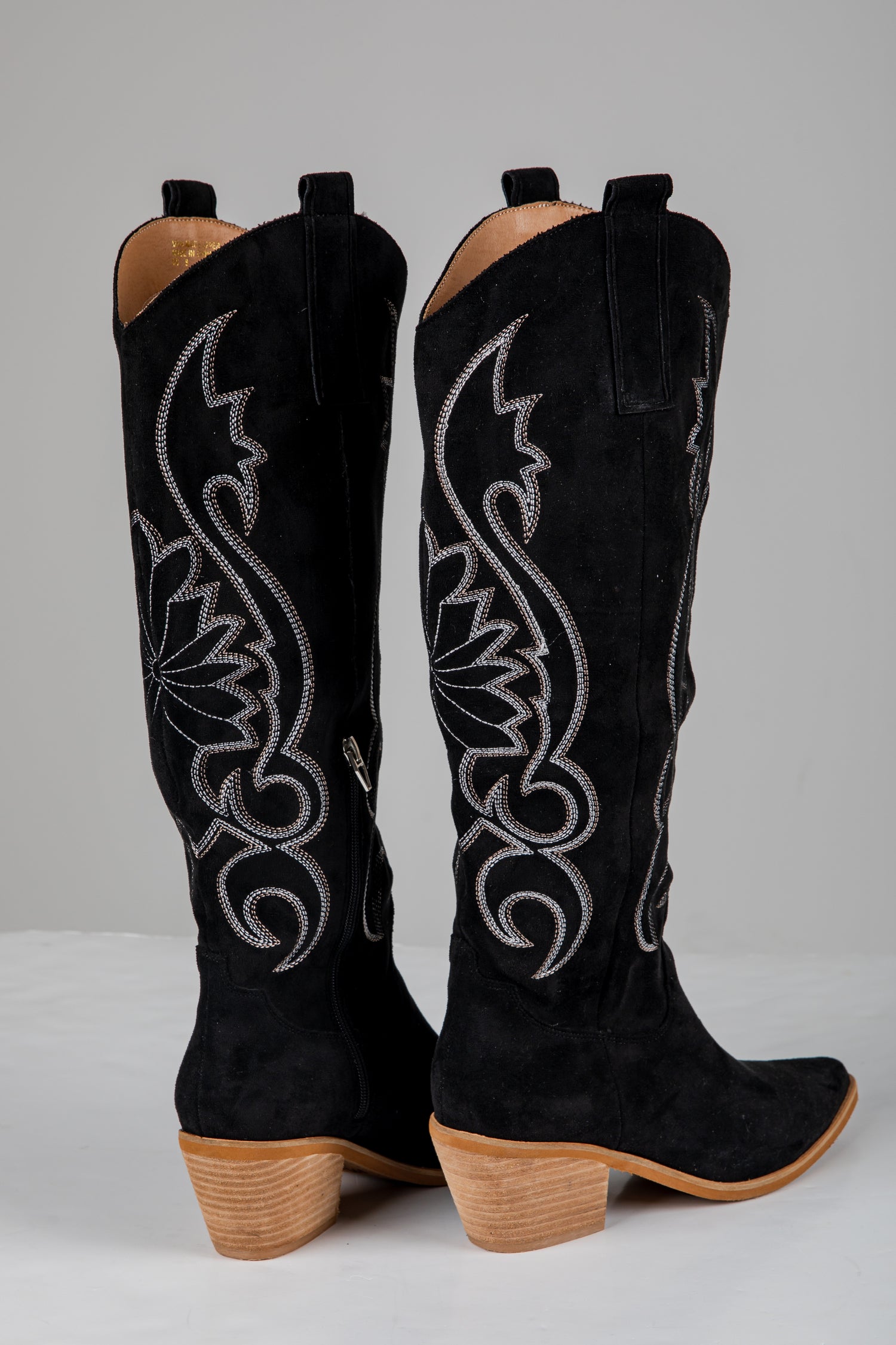 Black cowboy boots with intricate white embroidery on a gray background
