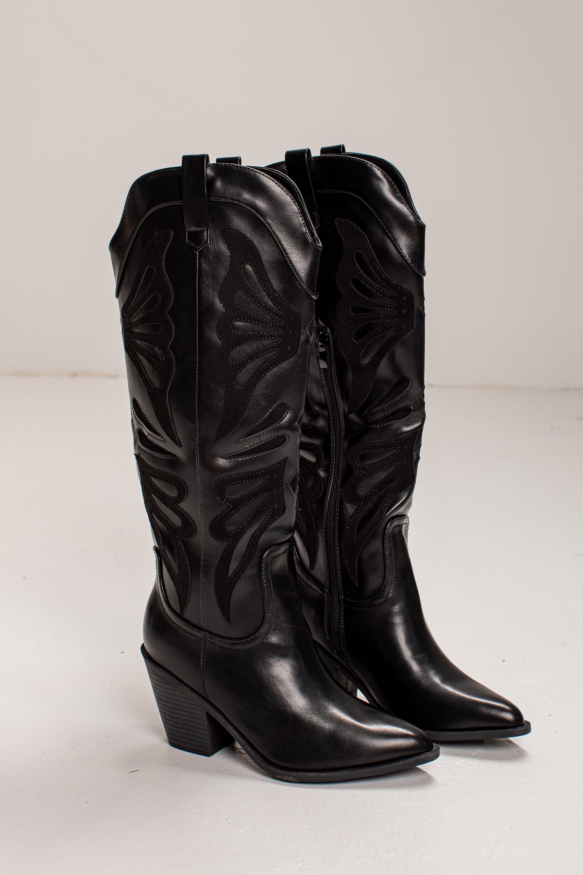 A pair of black leather cowboy boots with pointed toes, low block heels, and decorative floral embossing on the shafts, photographed against a plain light background.