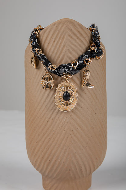 Bracelet with gold and black charms on a brown textured stand