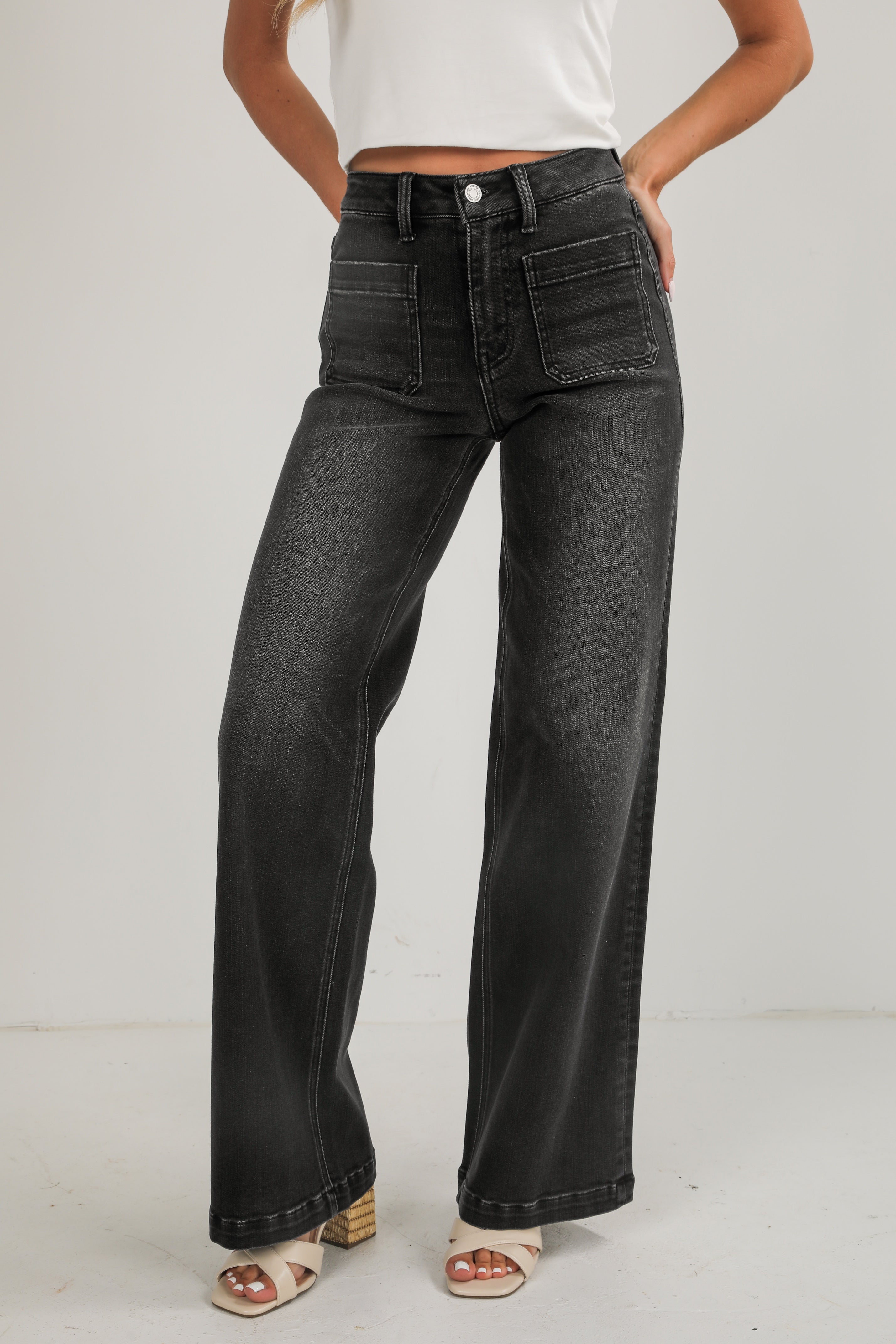 Person wearing black wide-leg jeans and a white top on a plain background