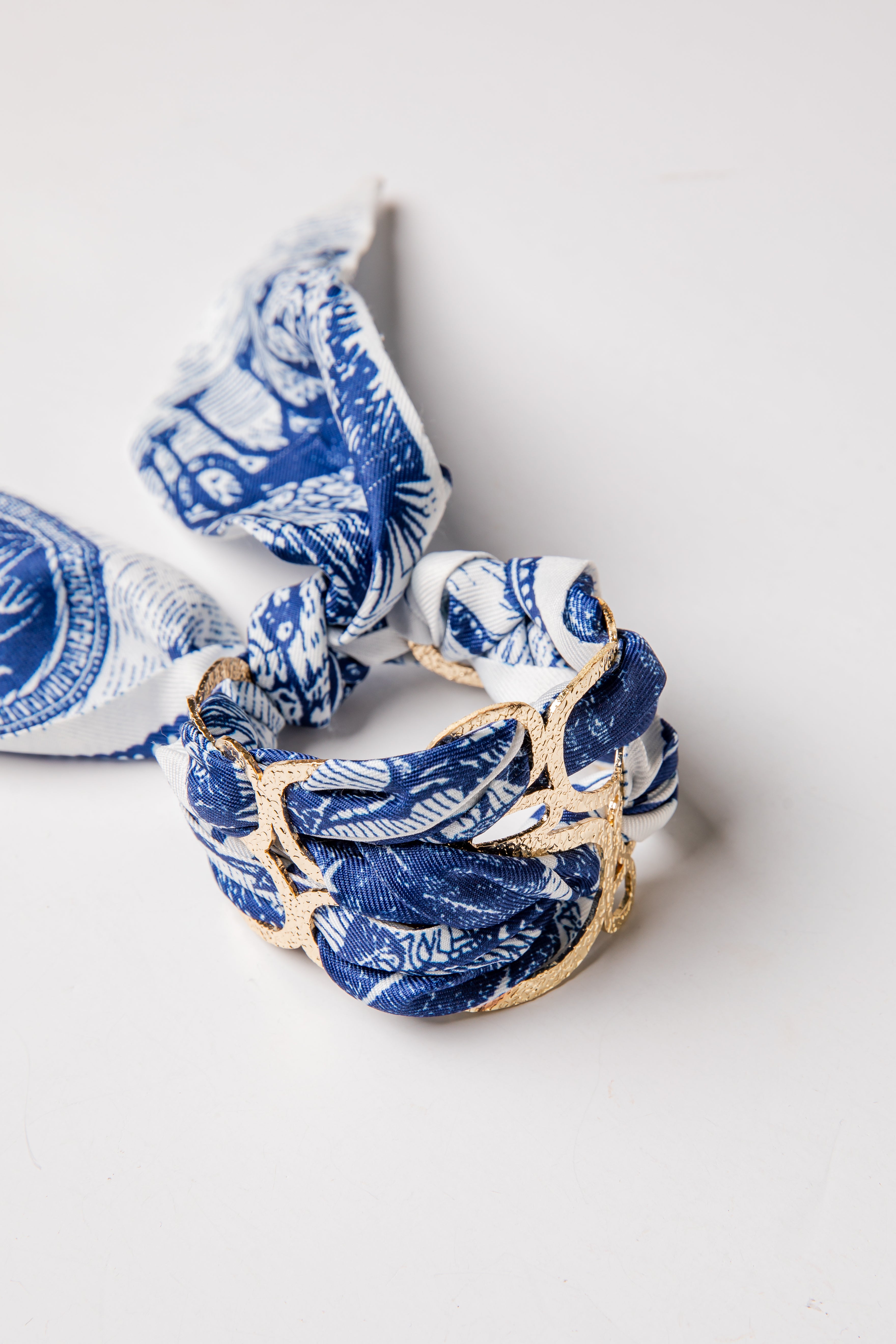 Blue and white patterned scarf with gold accents on a light gray background