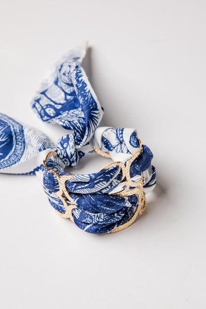 Blue and white patterned scarf with gold accents on a light gray background