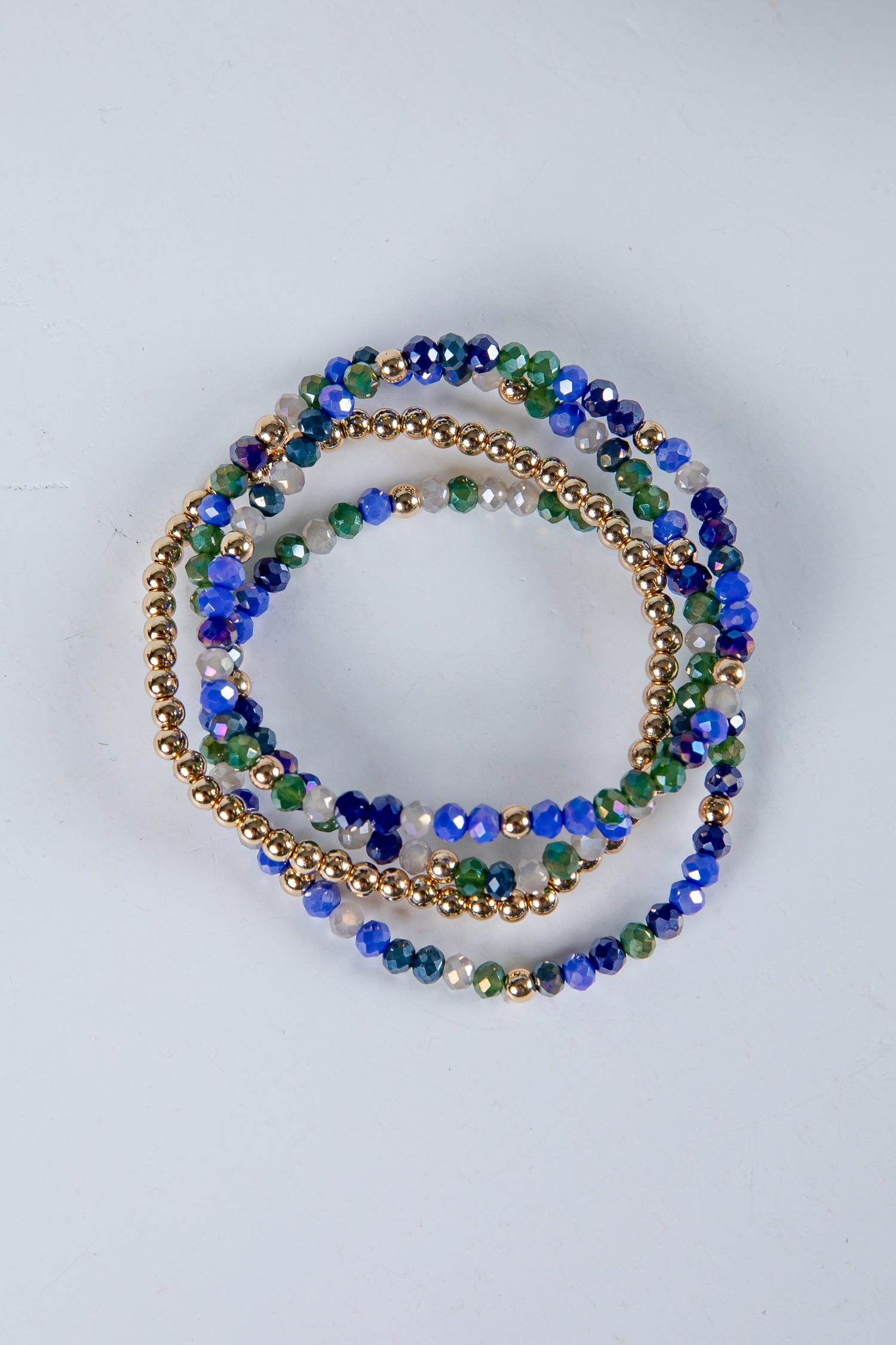 Set of beaded bracelets in blue, green, and gold on a light gray background
