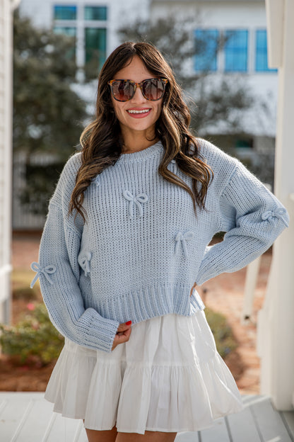Woman wearing a light blue sweater and white skirt outdoors