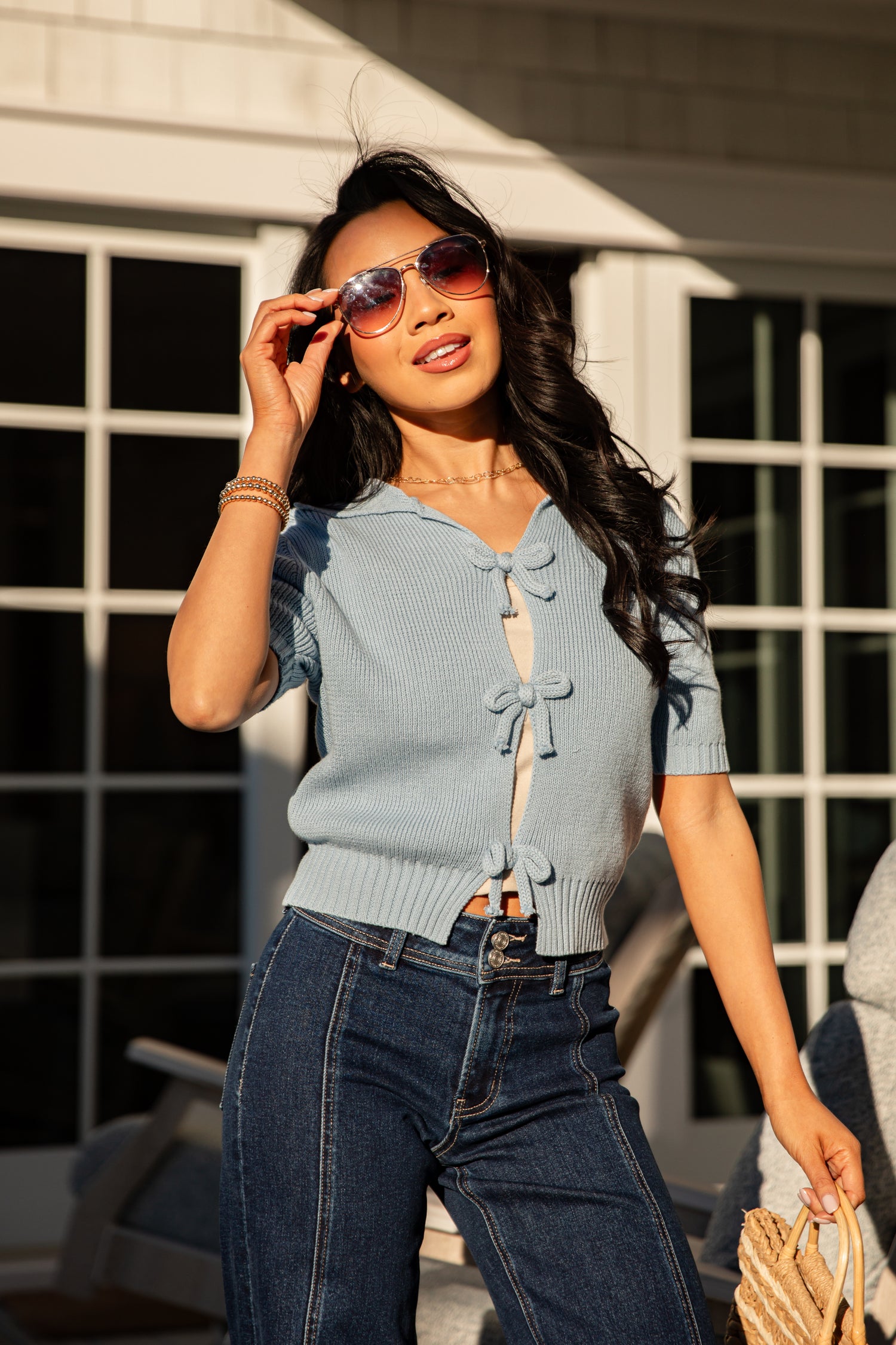 Woman wearing a light blue cardigan and dark jeans, standing outdoors.