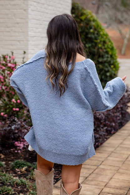 Woman wearing a blue sweater and beige boots walking outdoors.