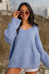 Woman wearing a light blue sweater and sunglasses outdoors with a beach-like background