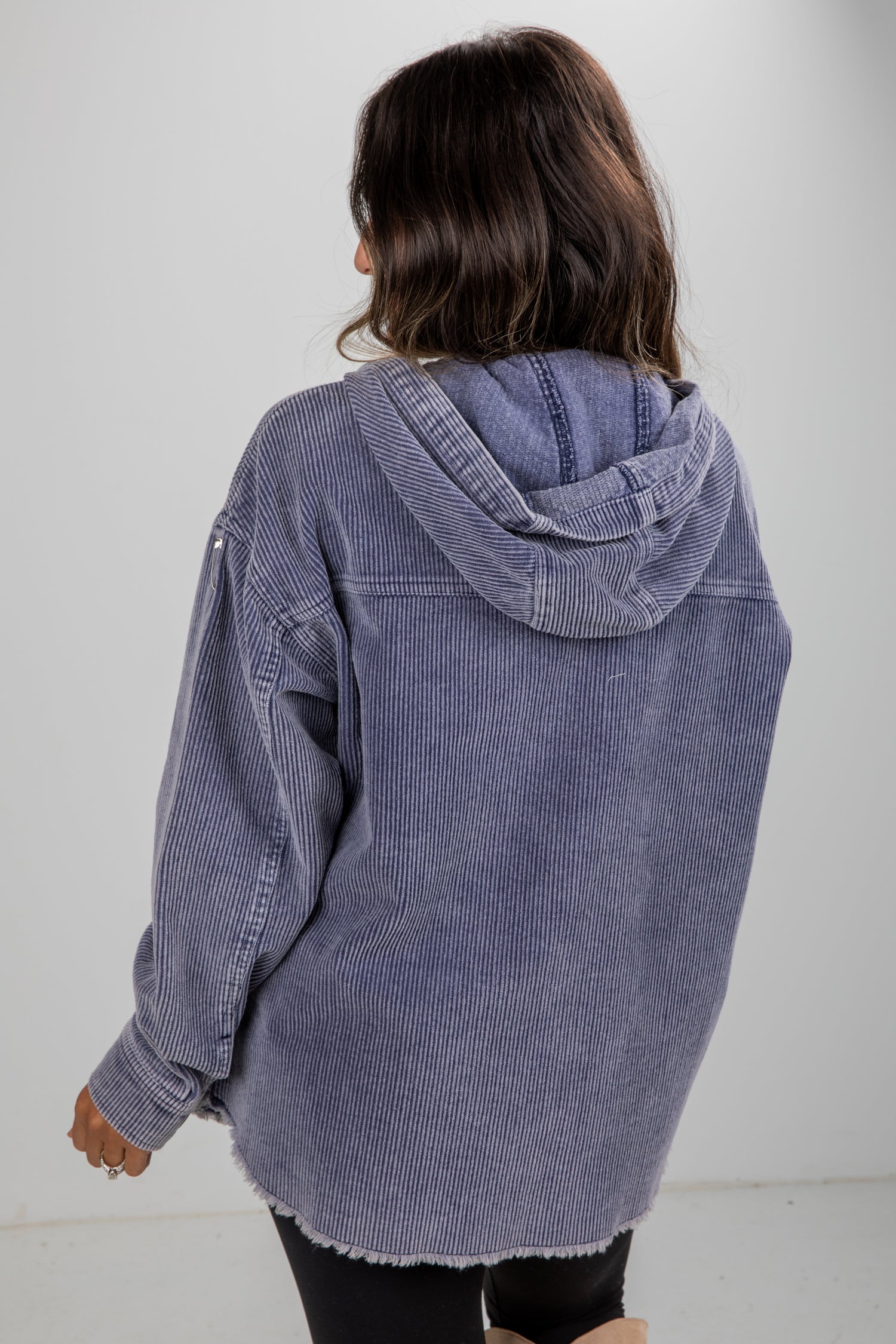 Person wearing a blue corduroy jacket with a hood on a plain background