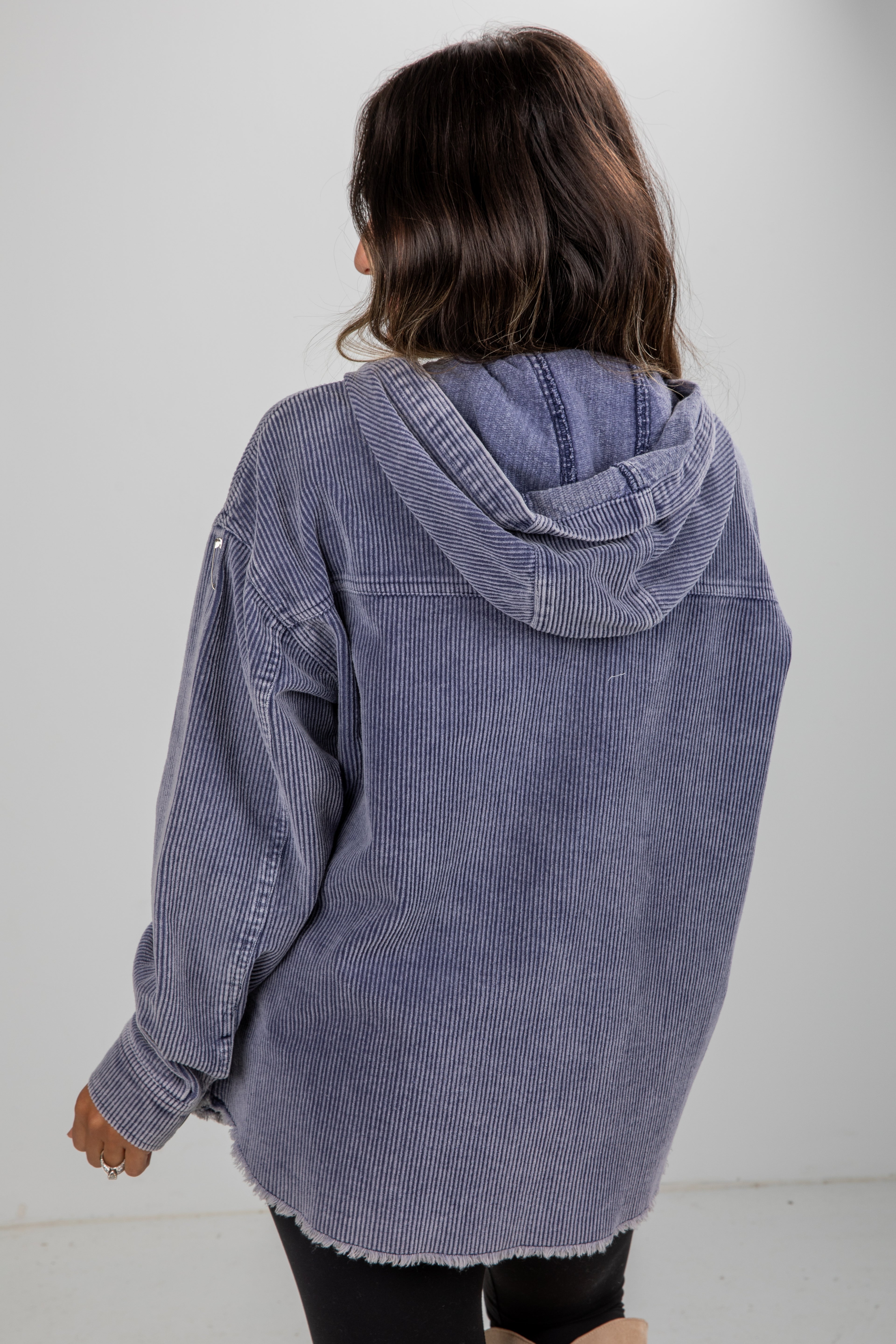 Person wearing a blue corduroy jacket with a hood on a plain background