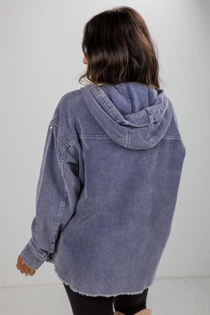 Person wearing a blue corduroy jacket with a hood on a plain background