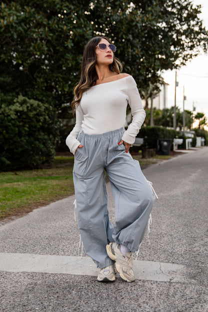 Woman in a white top and light blue pants standing on a road with trees in the background
