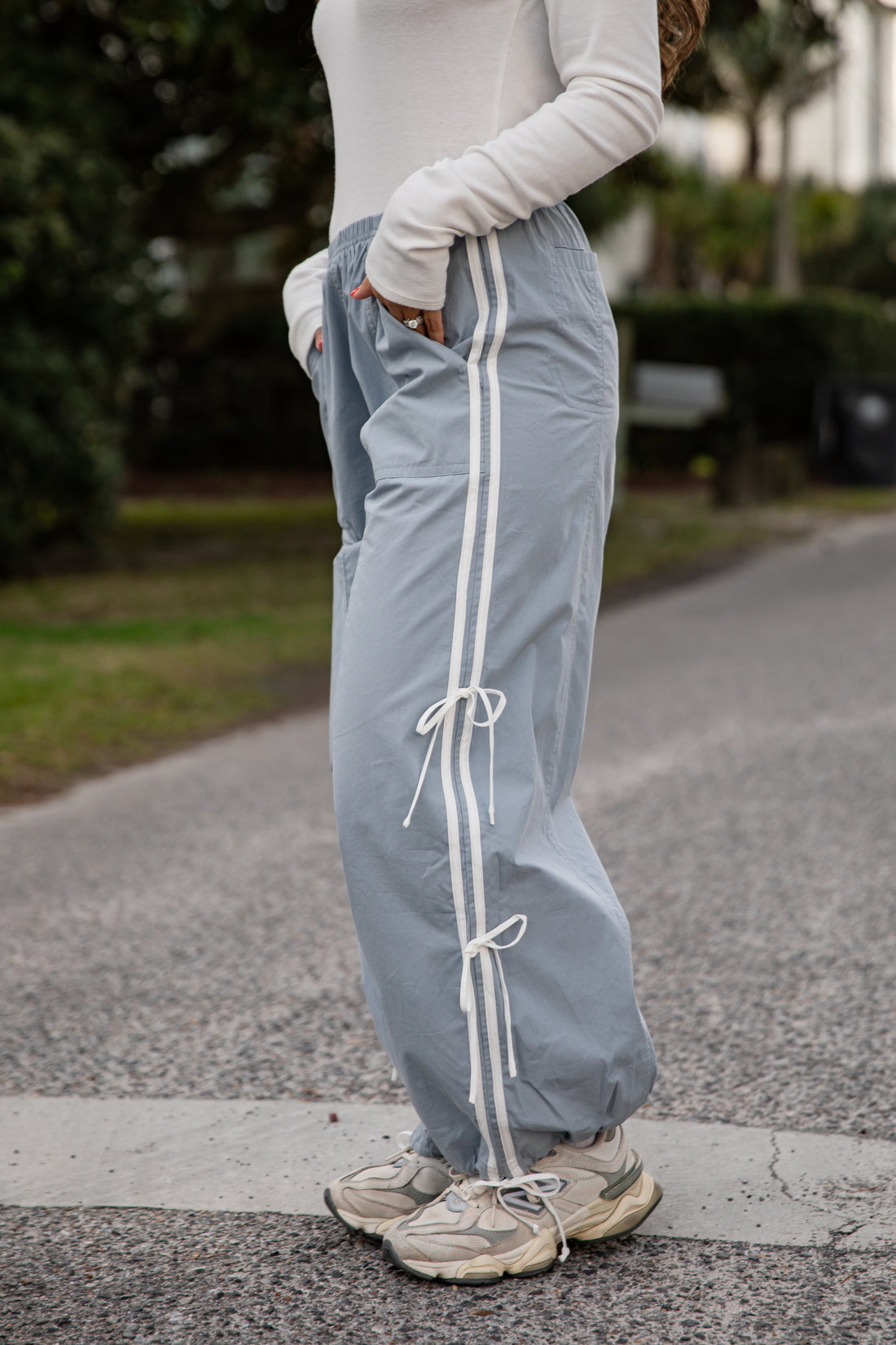 Person wearing light gray sweatpants with white drawstrings on a blurred outdoor background