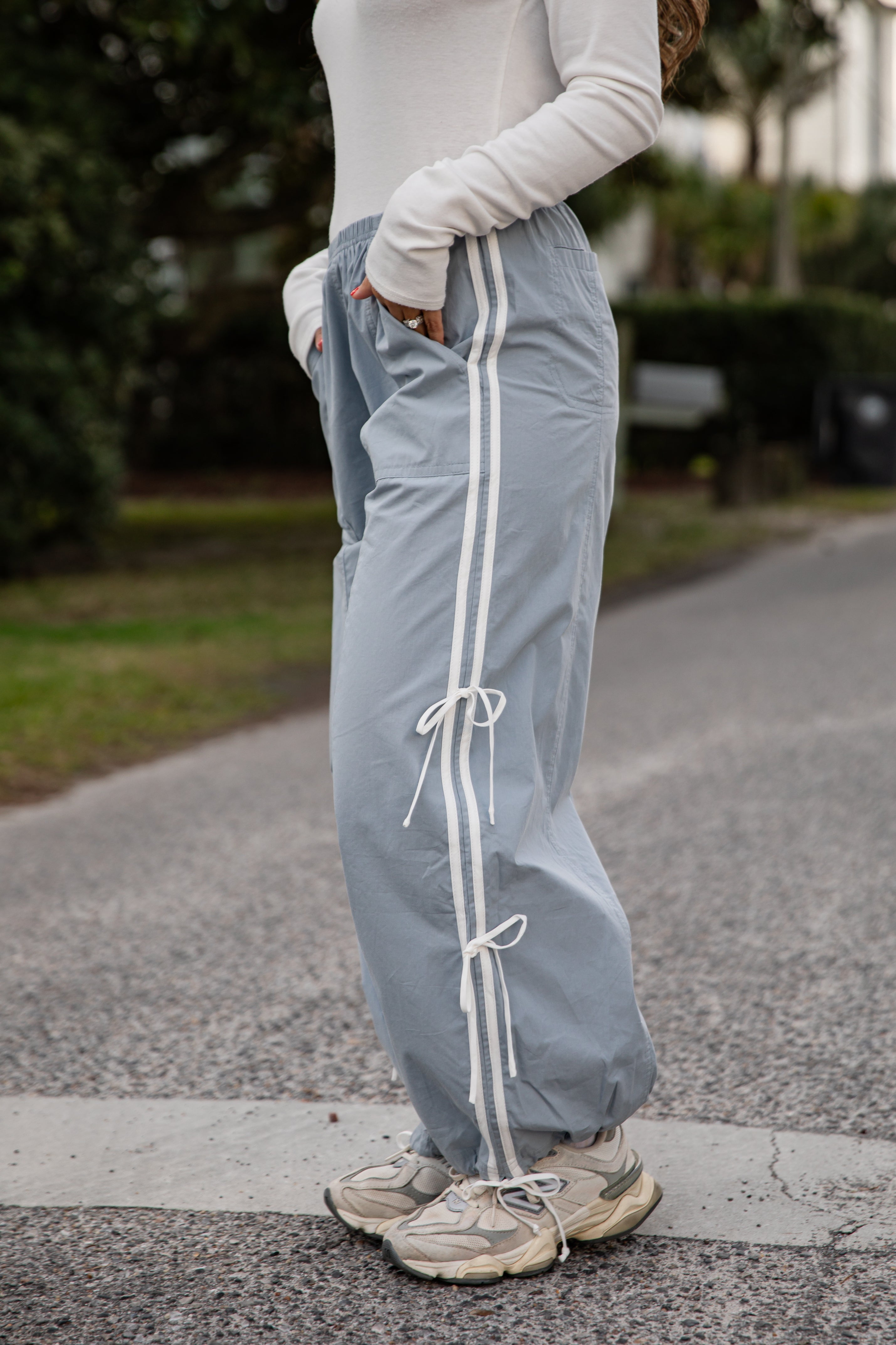 Person wearing light gray sweatpants with white drawstrings on a blurred outdoor background