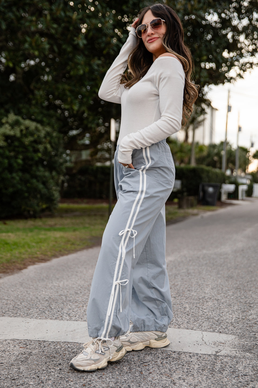 Woman wearing a white long-sleeve top and light blue track pants with white stripes on a road.