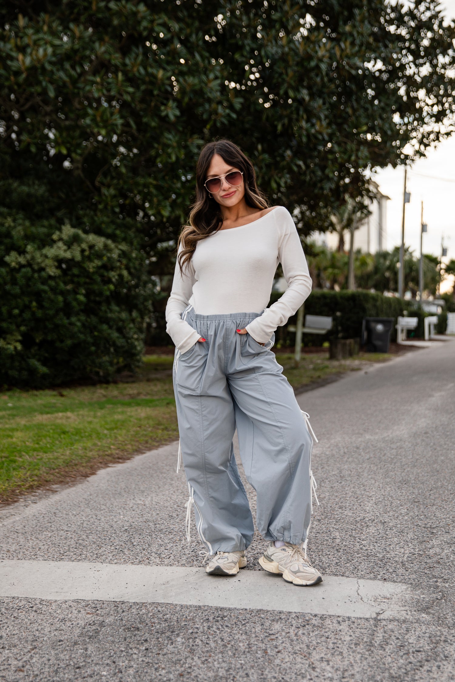 Woman wearing a white top and light blue pants standing on a path with trees in the background