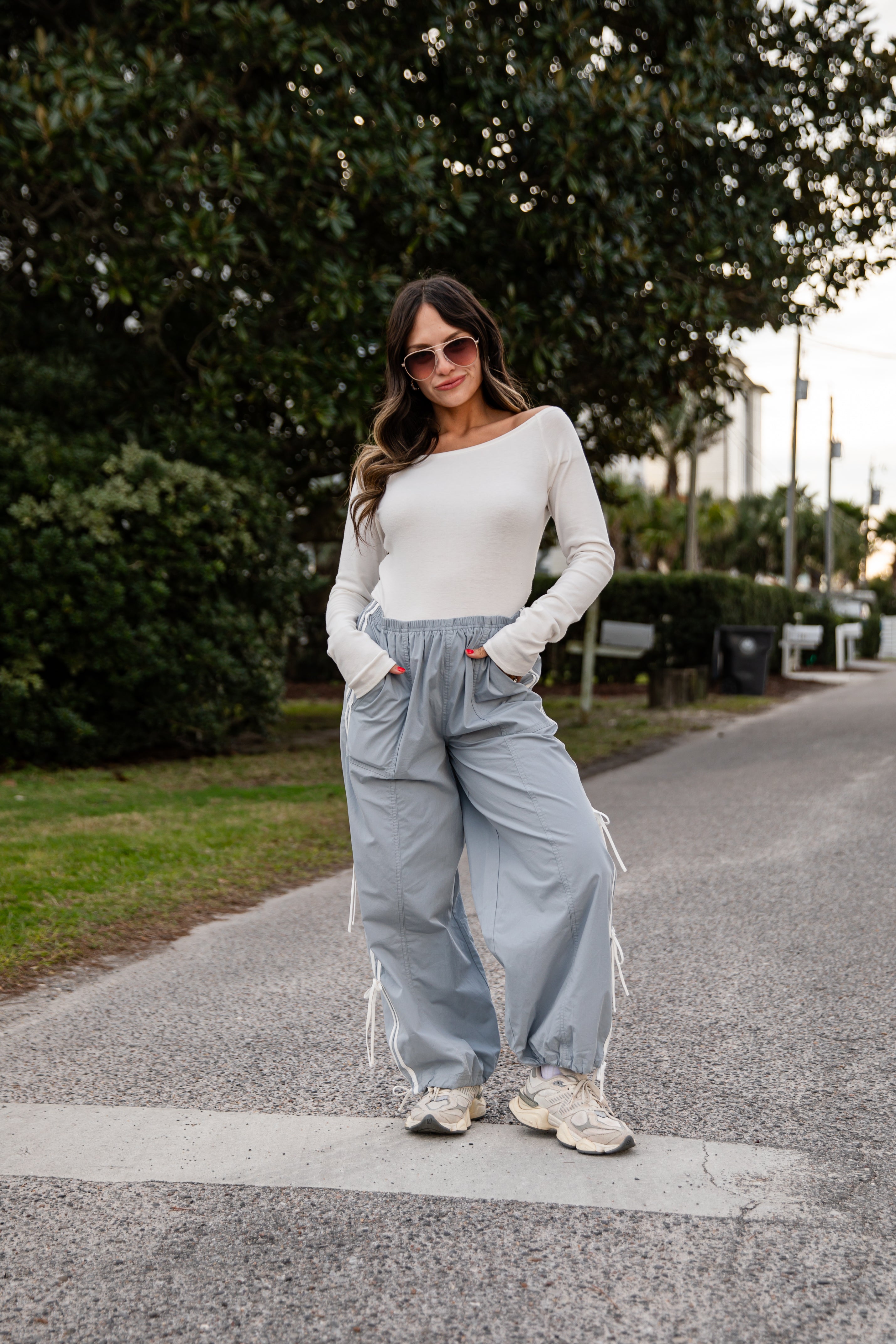 Woman wearing a white top and light blue pants standing on a path with trees in the background