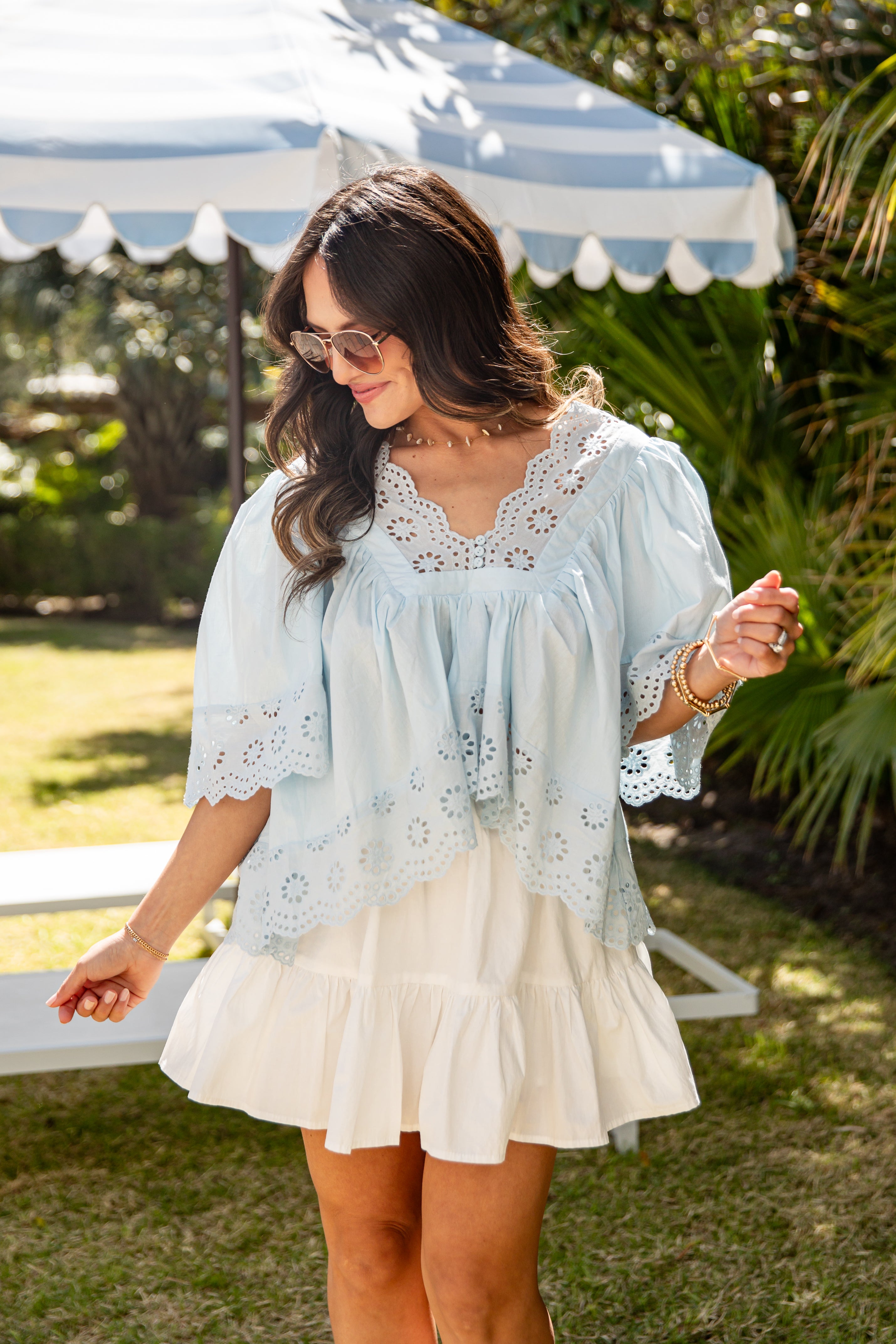 Woman wearing a light blue blouse with lace details and a white skirt outdoors.