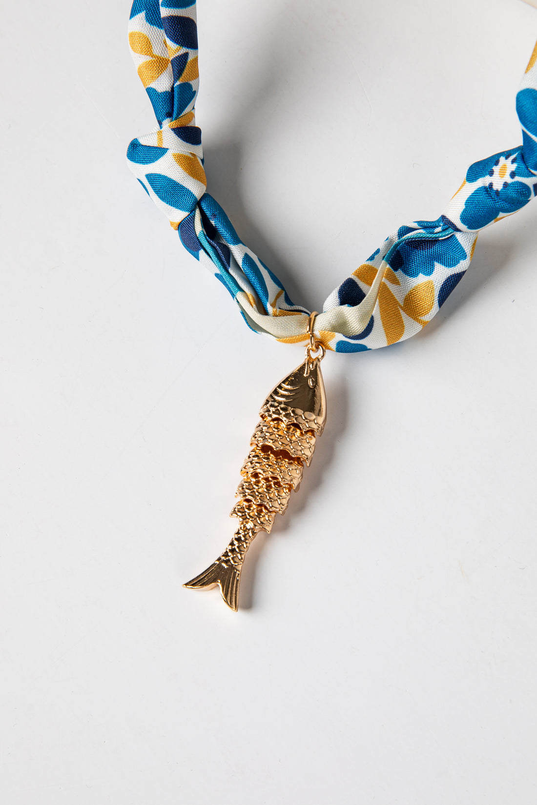 Necklace with a gold fish pendant on a floral-patterned ribbon against a white background
