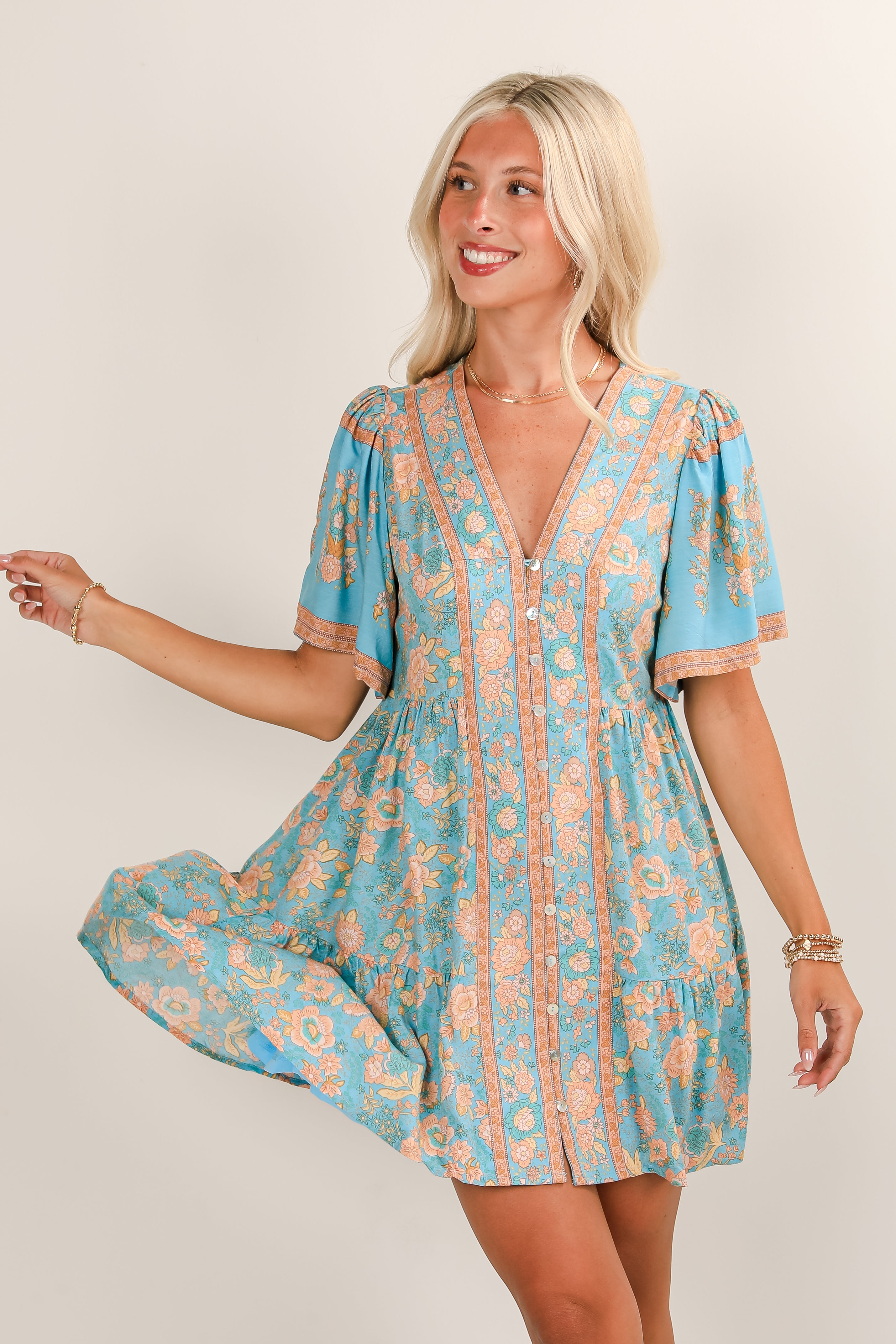 Woman wearing a blue and orange floral dress against a plain background