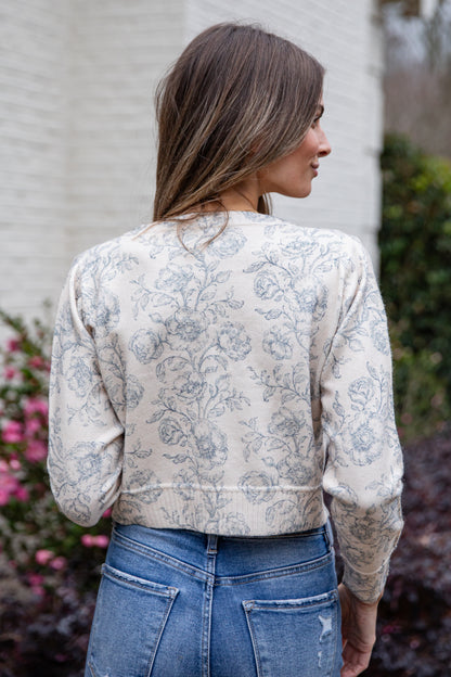 Woman wearing a floral blouse and blue jeans outdoors.