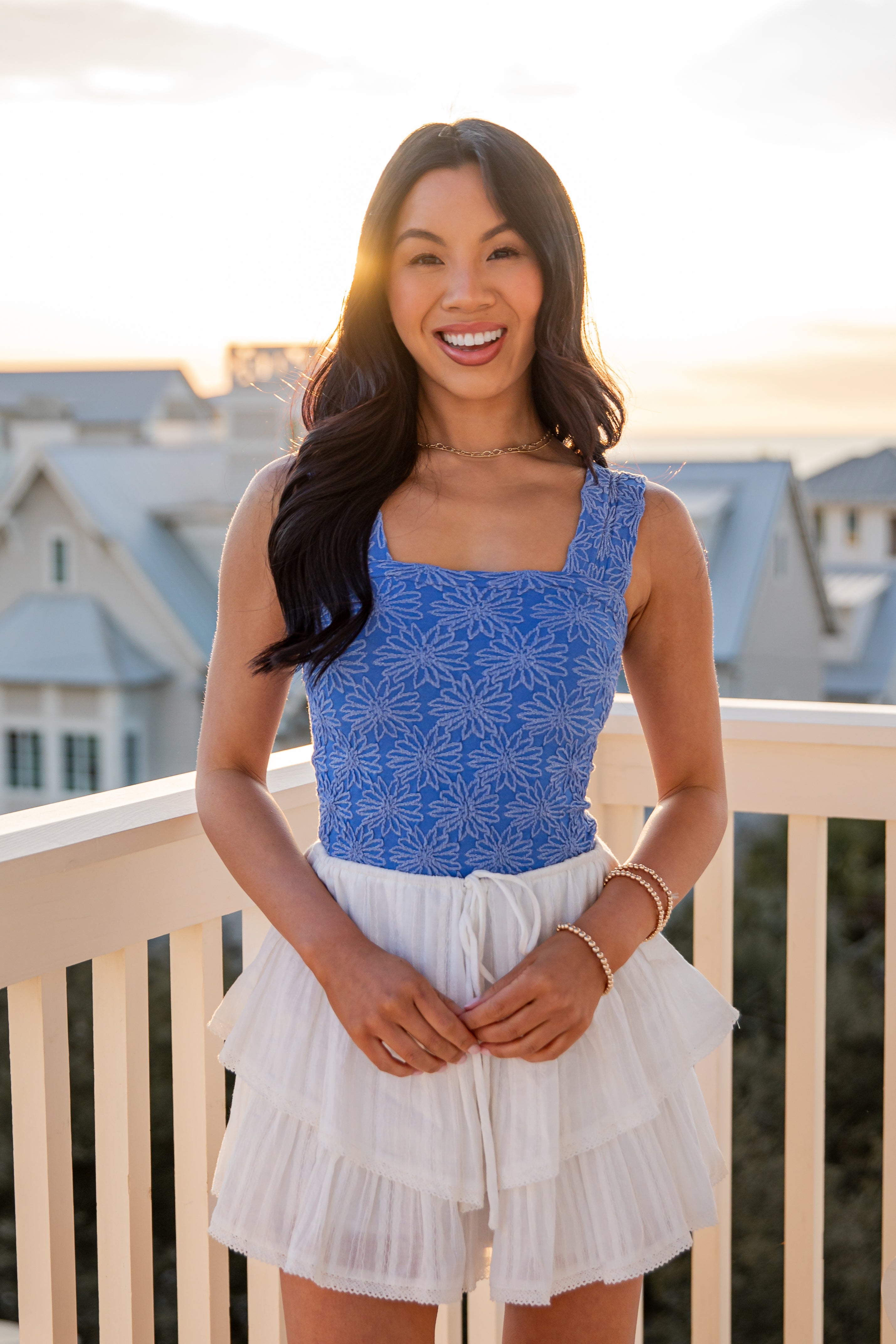 Woman wearing a blue top and white skirt on a balcony with a scenic background