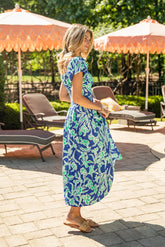 Woman in a blue floral dress standing on a patio with orange umbrellas and lounge chairs.