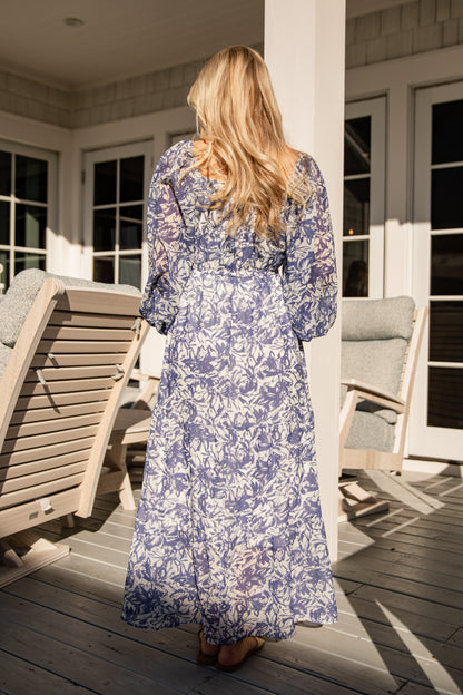 Woman in a blue floral dress standing on a wooden deck.