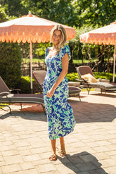 Woman in a blue floral dress standing in a sunlit outdoor setting with umbrellas and lounge chairs.