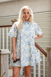 Woman wearing a floral dress standing outdoors near a staircase.